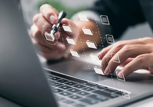 A person working on a laptop with icons appearing projected from the screen.
