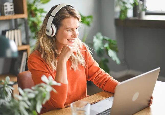 A woman wearing headphones working on a laptop.