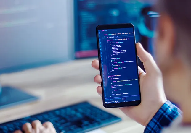 A person holding a phone with JavaScript code displayed on the screen.