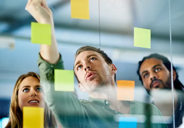 Three people posting post-it notes on a transparent glass wall.