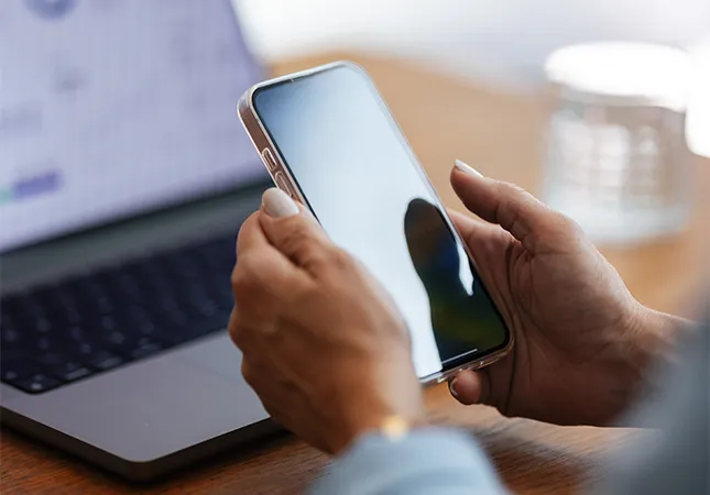 A person holding a phone in front of a laptop.