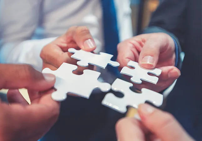 Four hands hold four pieces of a jigsaw that fit together.