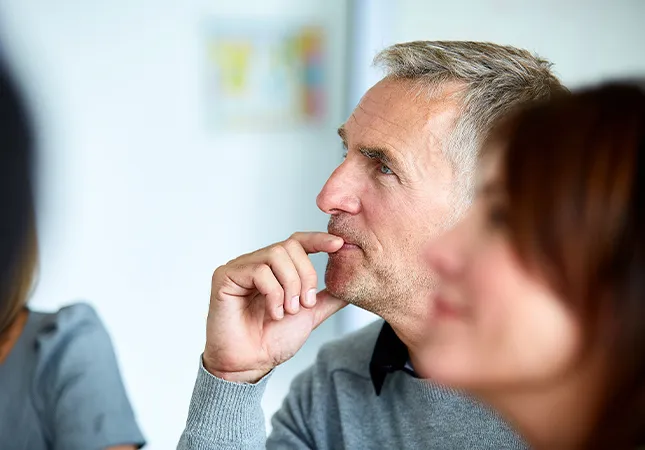 A man sits next to a woman with this hand on his chin as he thinks.